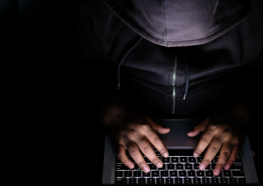 young person typing on a laptop with their hood up hiding their face