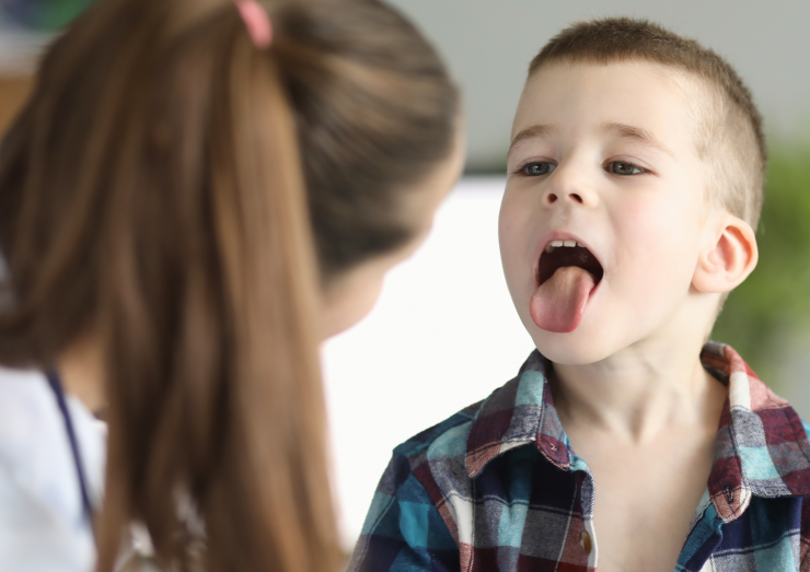 boy with tongue out whilst doctor looks inside his mouth